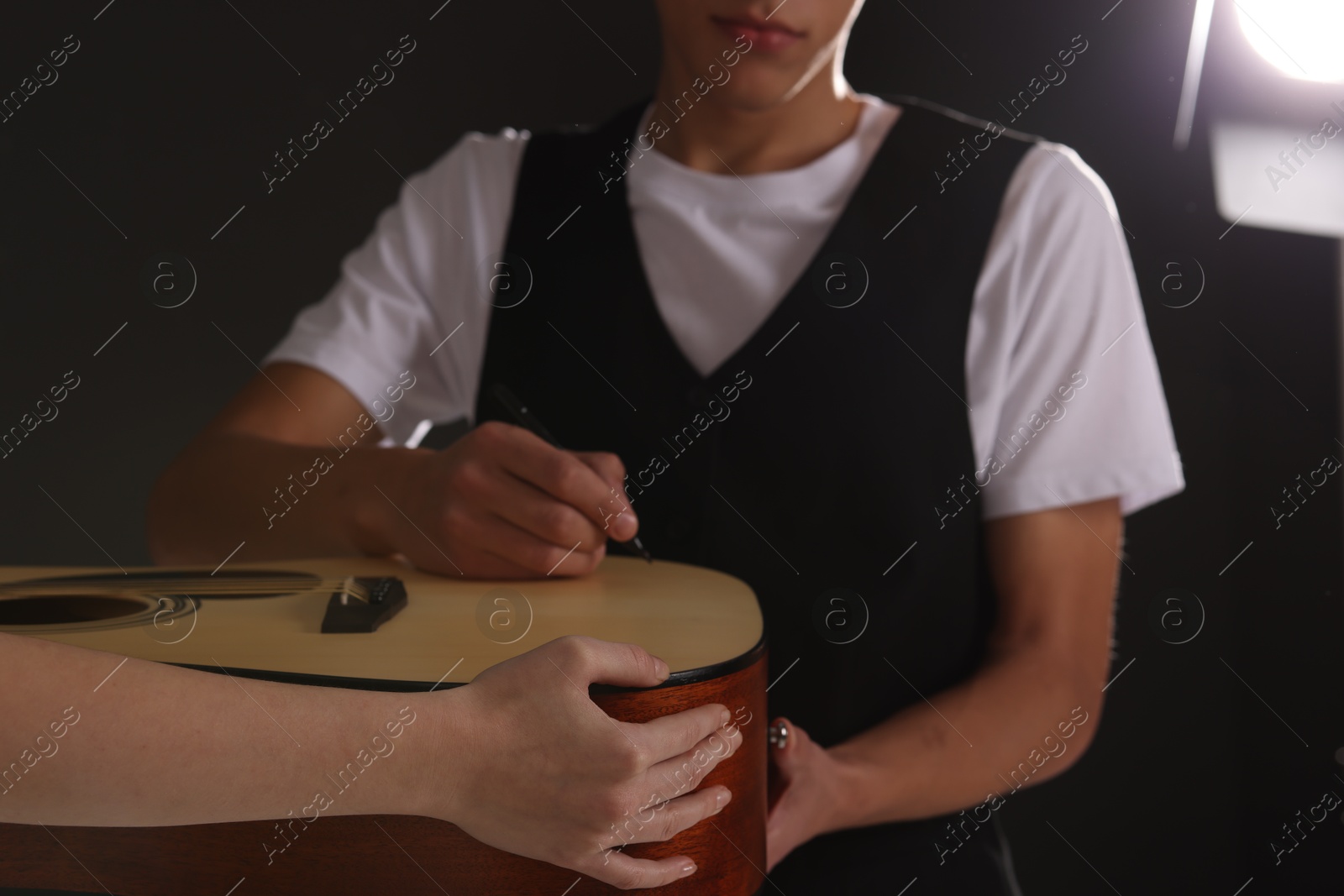 Photo of Musician signing autograph on guitar against dark background, closeup