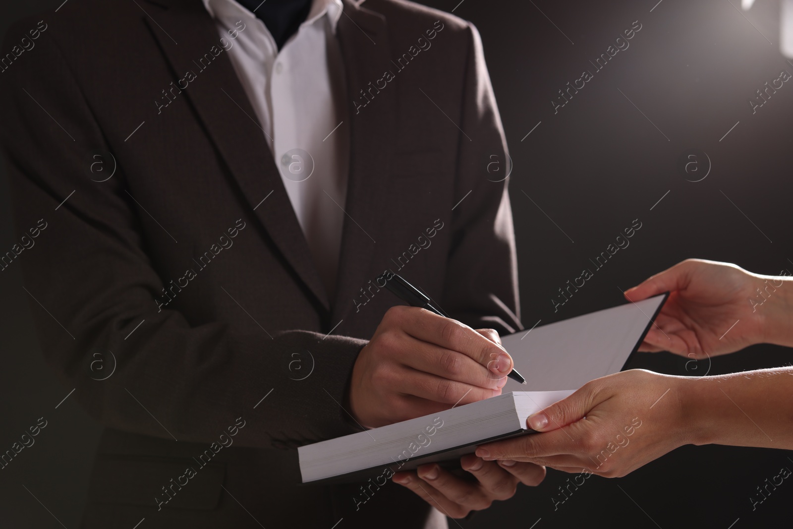 Photo of Writer signing autograph in book on dark background, closeup