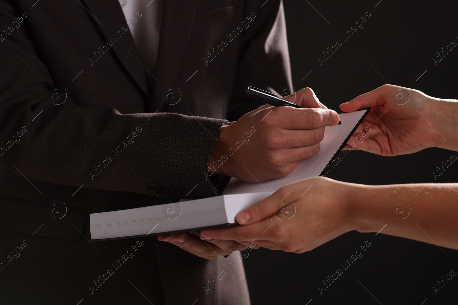 Photo of Writer signing autograph in book on black background, closeup