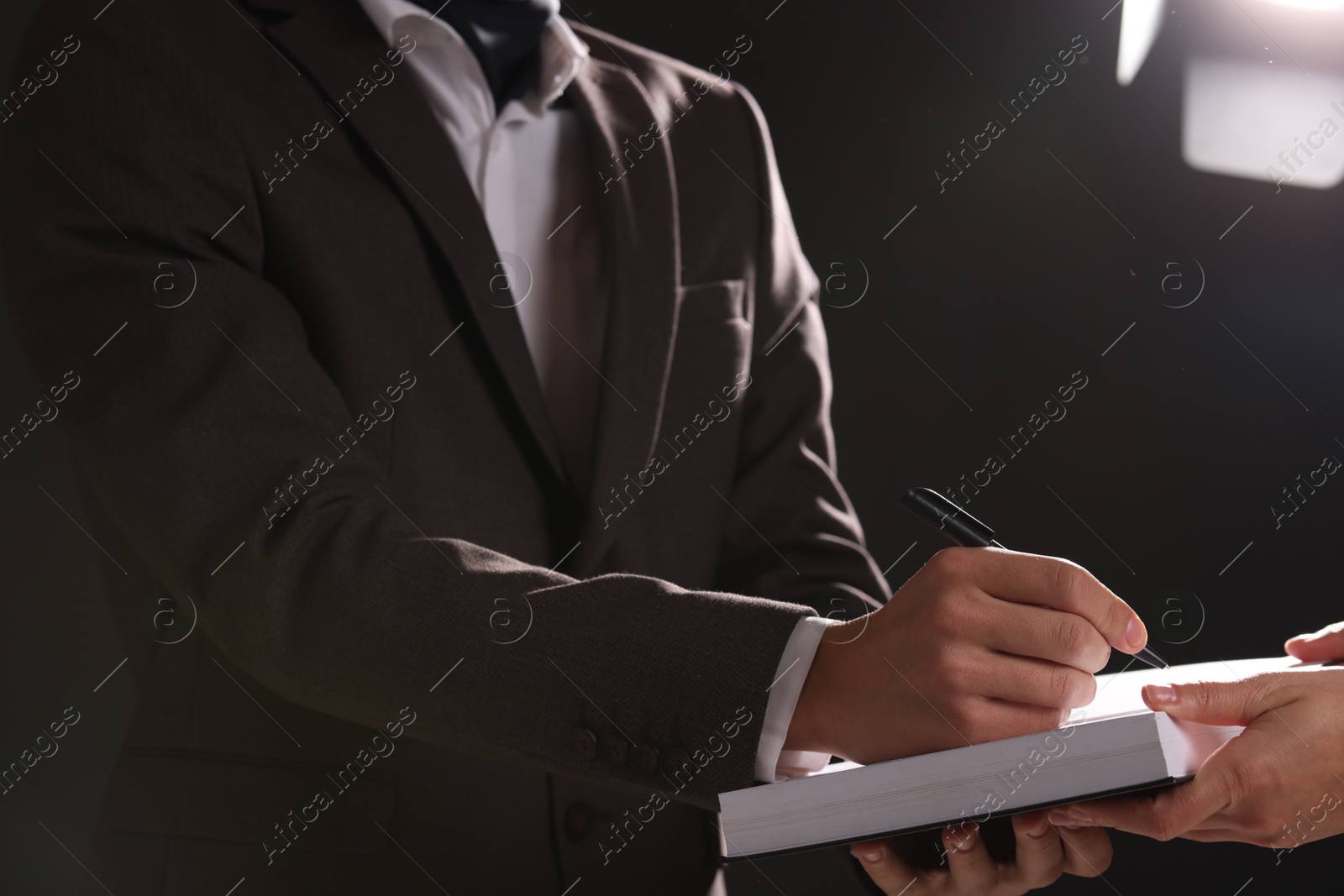 Photo of Writer signing autograph in book on dark background, closeup