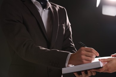 Photo of Writer signing autograph in book on dark background, closeup