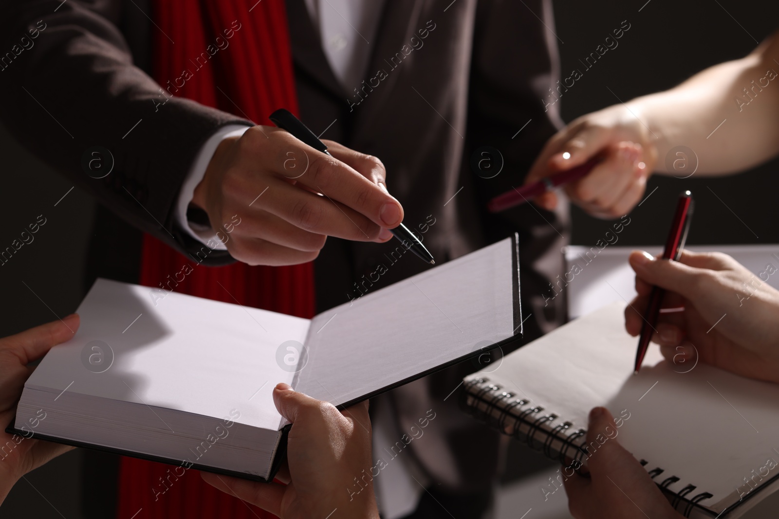 Photo of Man signing autograph in book on dark background, closeup