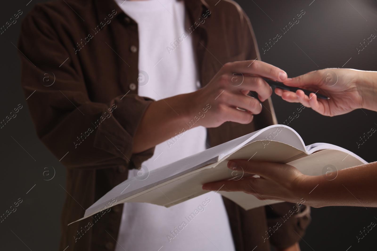 Photo of Man signing autograph in notebook on black background, closeup