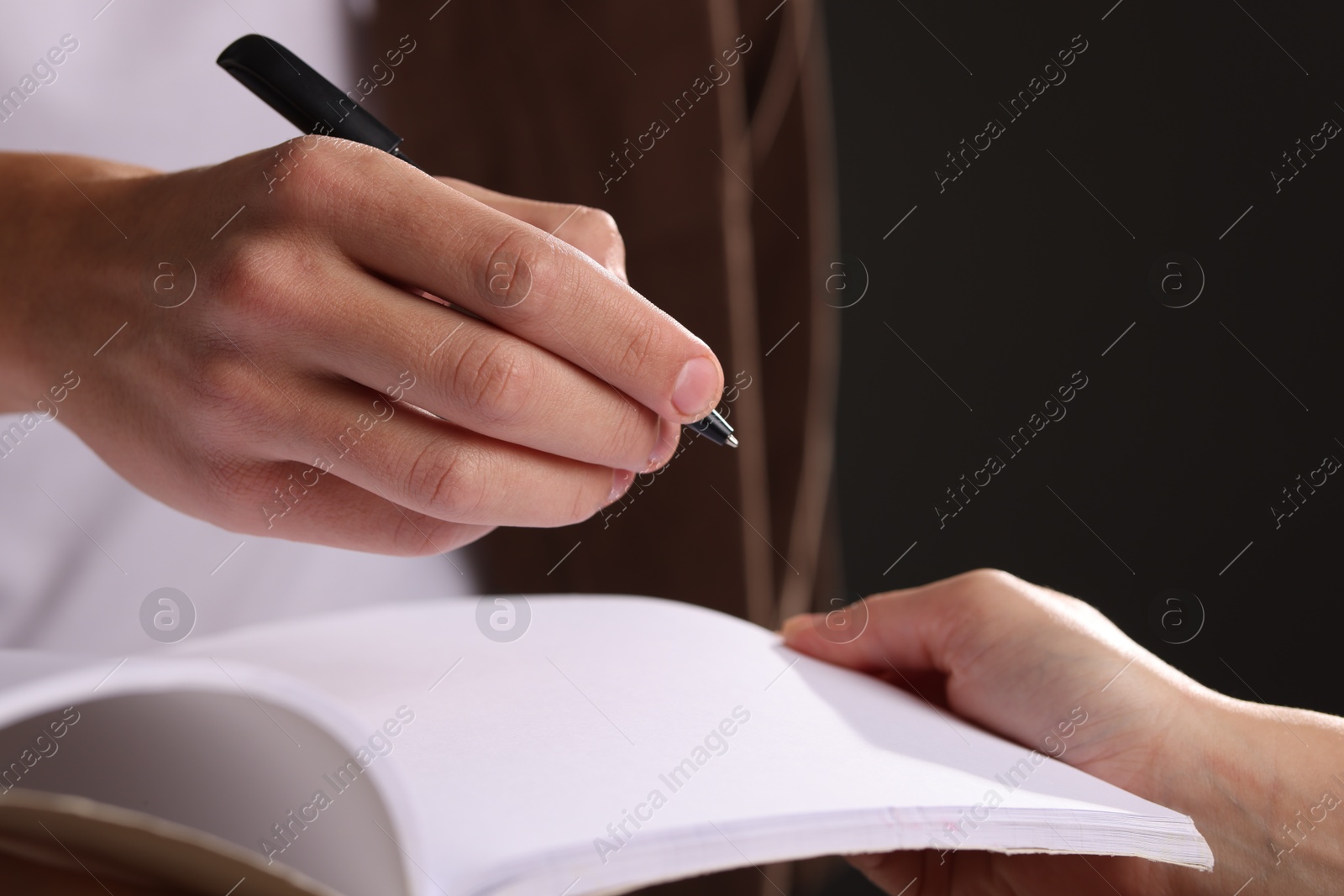 Photo of Man signing autograph in notebook on black background, closeup