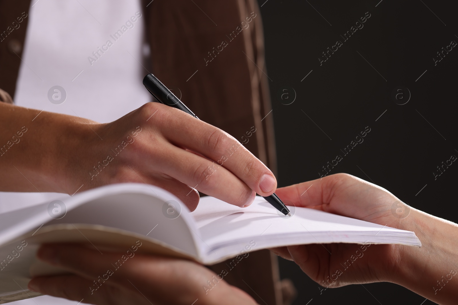 Photo of Man signing autograph in notebook on black background, closeup