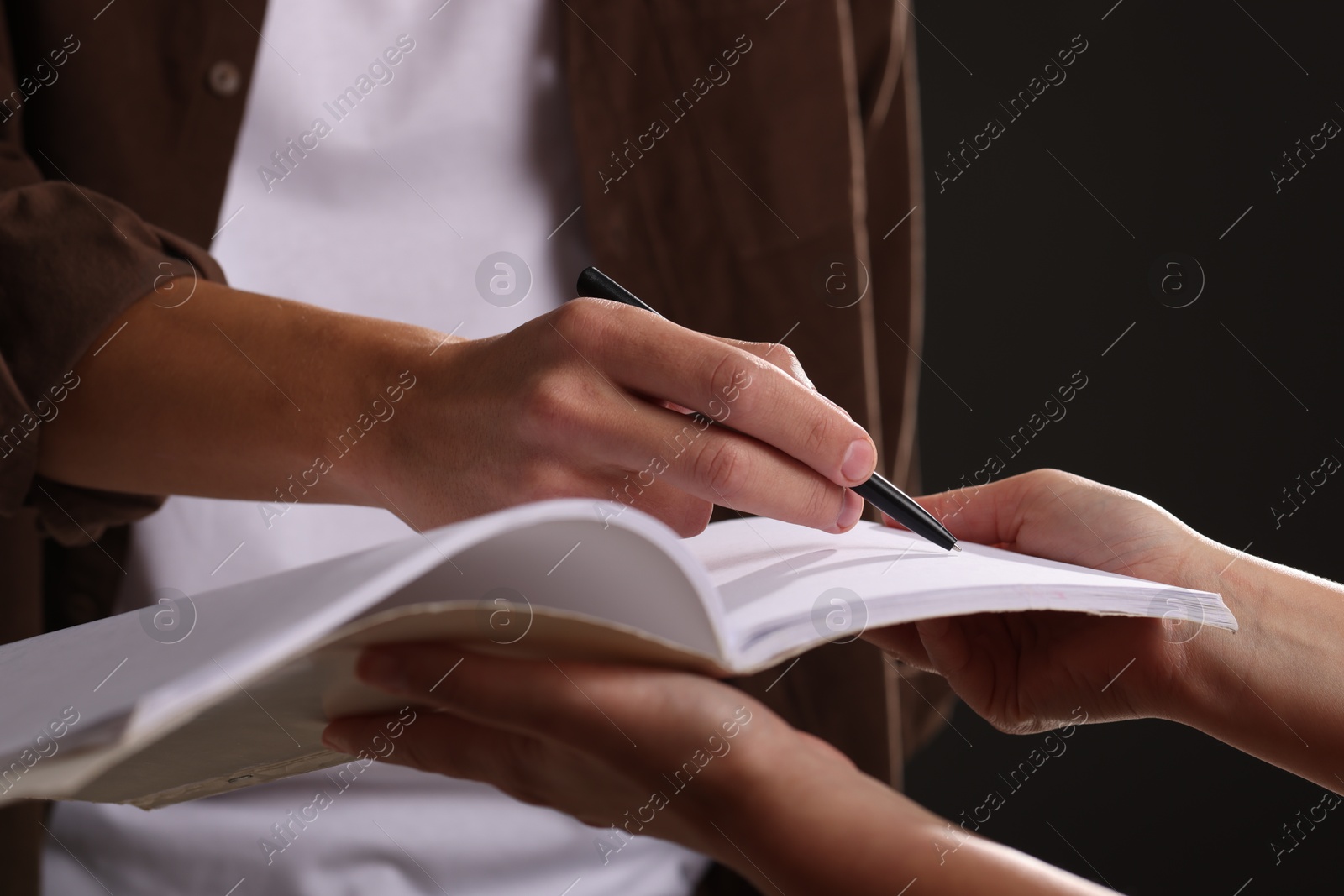 Photo of Man signing autograph in notebook on black background, closeup