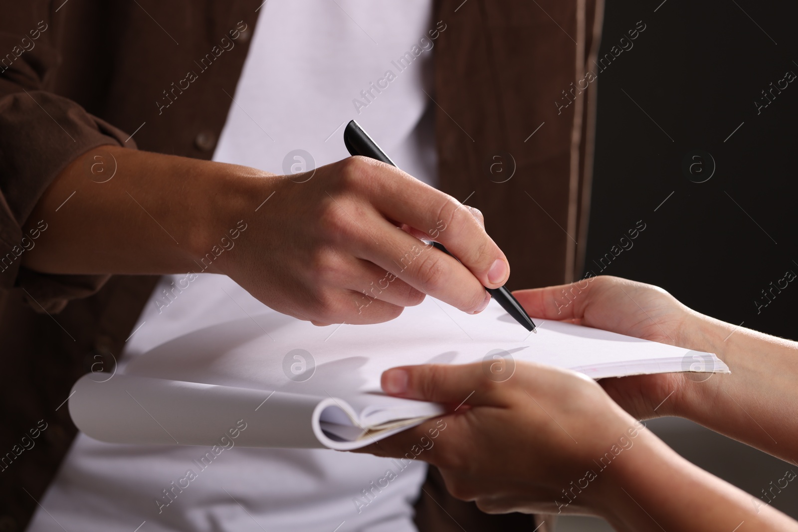 Photo of Man signing autograph in notebook on black background, closeup