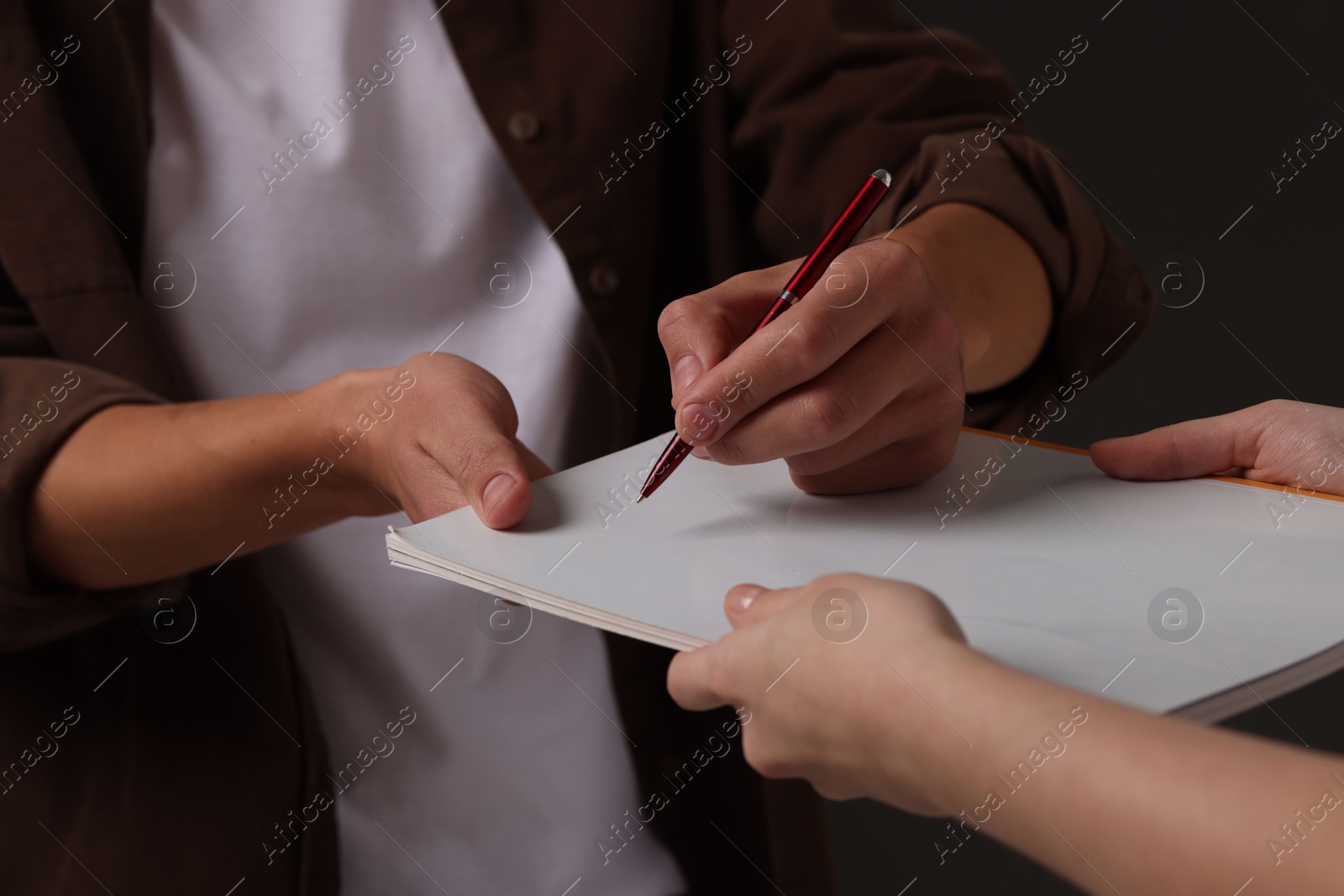 Photo of Man signing autograph in notebook on black background, closeup