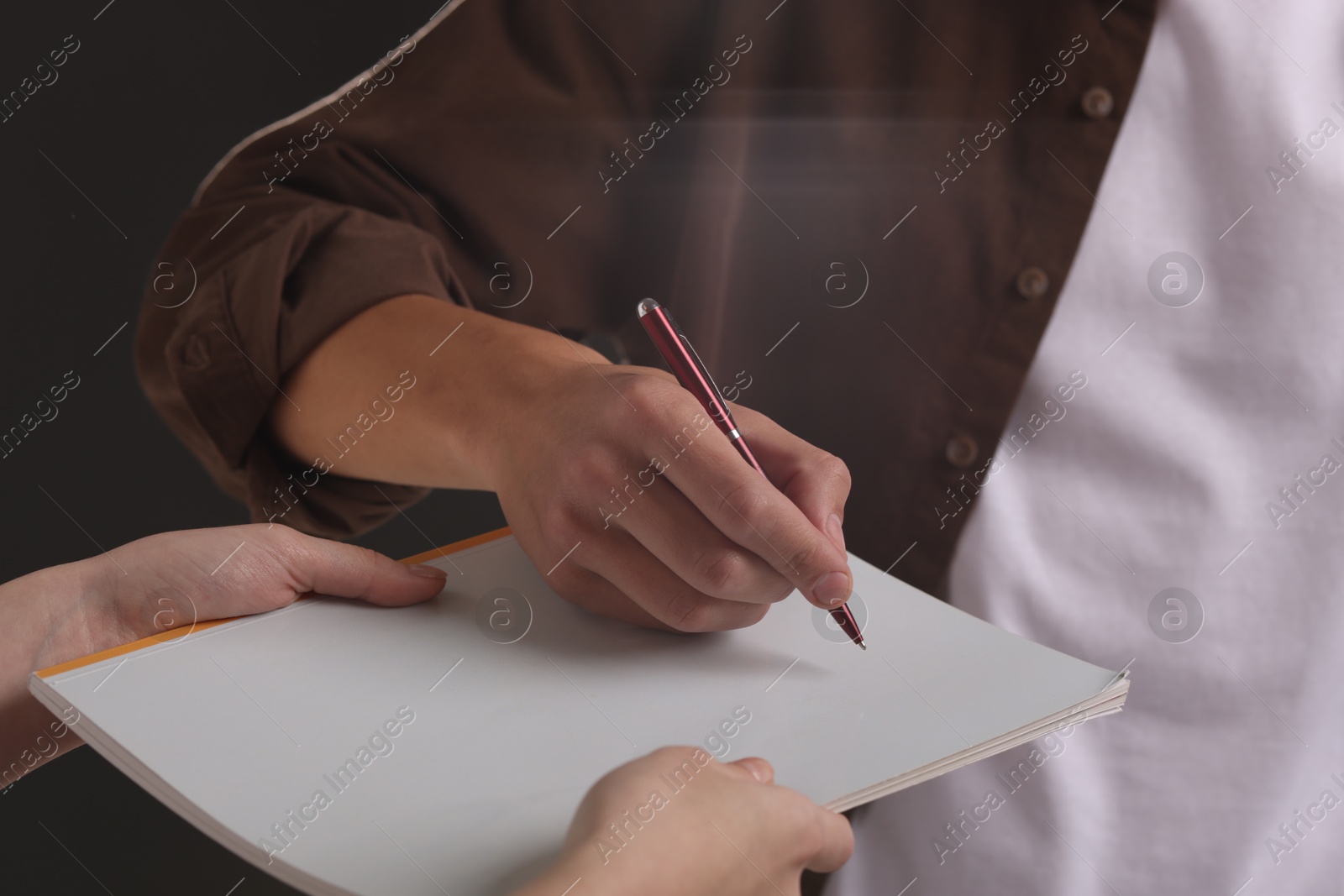 Photo of Man signing autograph in notebook on black background, closeup