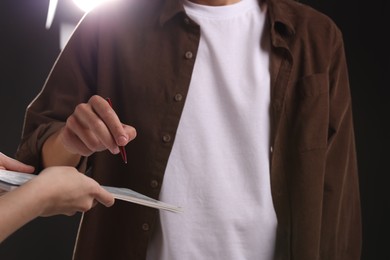 Photo of Man signing autograph in notebook on dark background, closeup