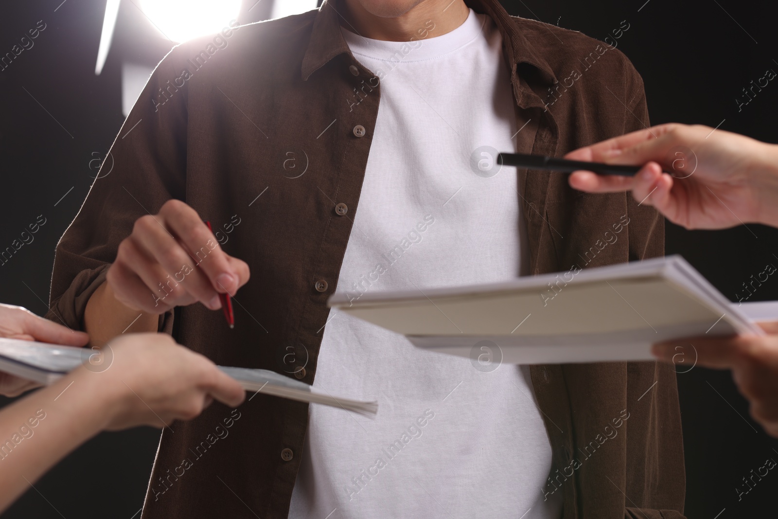 Photo of Man signing autograph in notebook on dark background, closeup