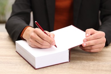 Writer signing autograph in book at wooden table indoors, closeup