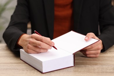 Photo of Writer signing autograph in book at wooden table indoors, closeup