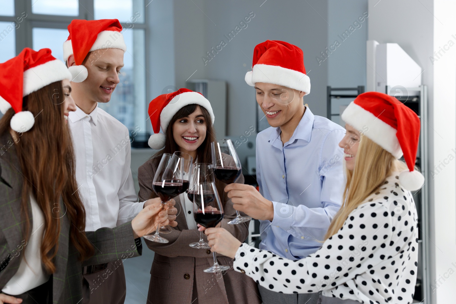 Photo of Happy coworkers clinking glasses of wine during office Christmas party