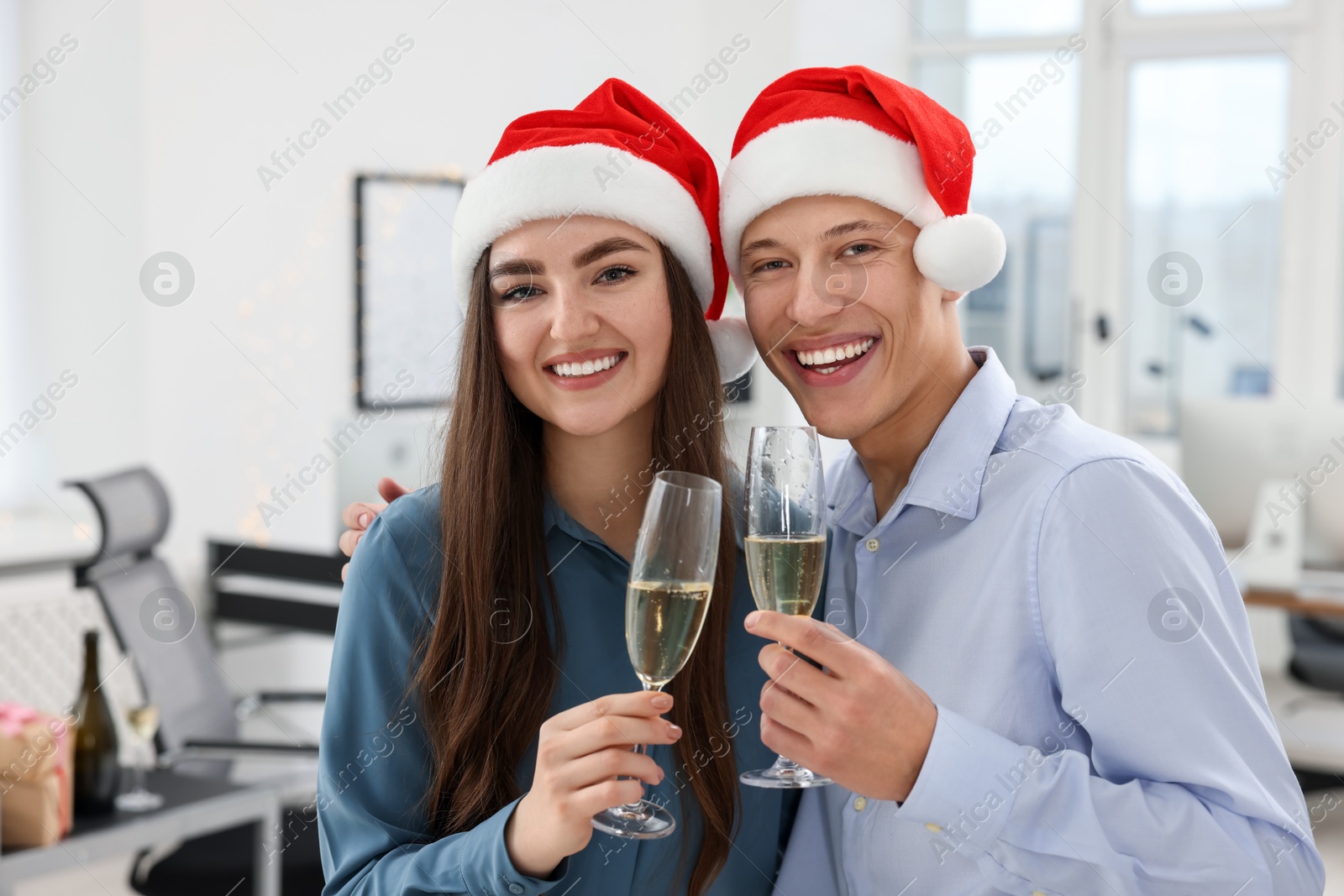 Photo of Cheerful coworkers in Santa hats with glasses of wine at office Christmas party