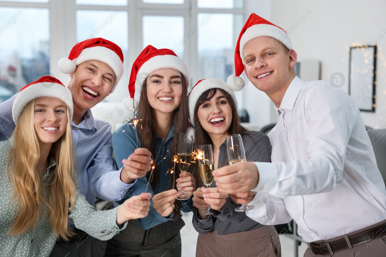 Photo of Happy colleagues with sparklers and glasses of wine at Christmas party in office