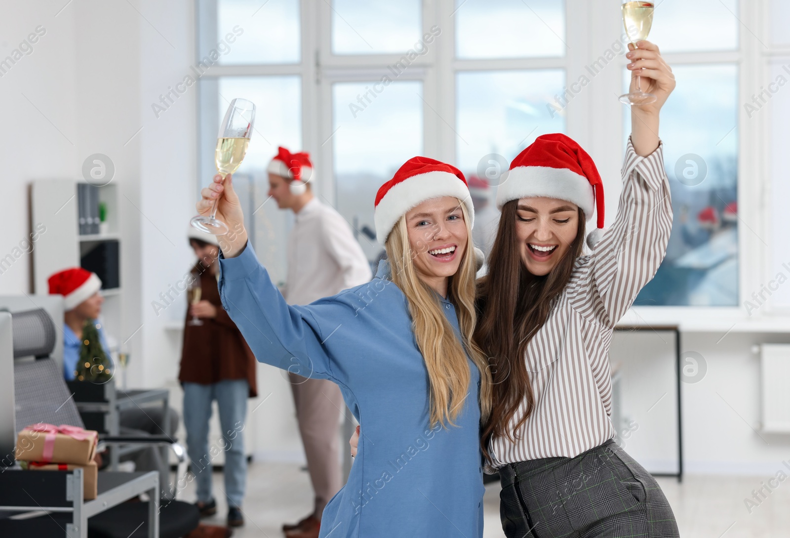 Photo of Smiling colleagues in Santa hats with wine enjoying office Christmas party