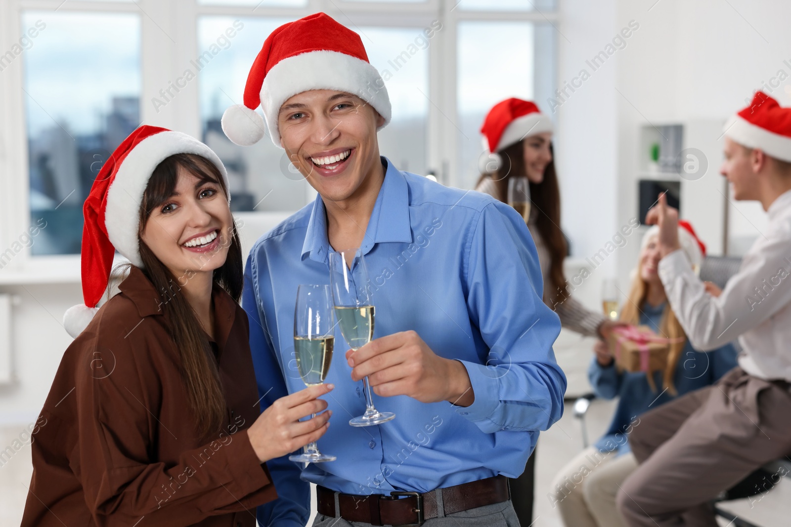 Photo of Smiling colleagues in Santa hats with wine at office Christmas party