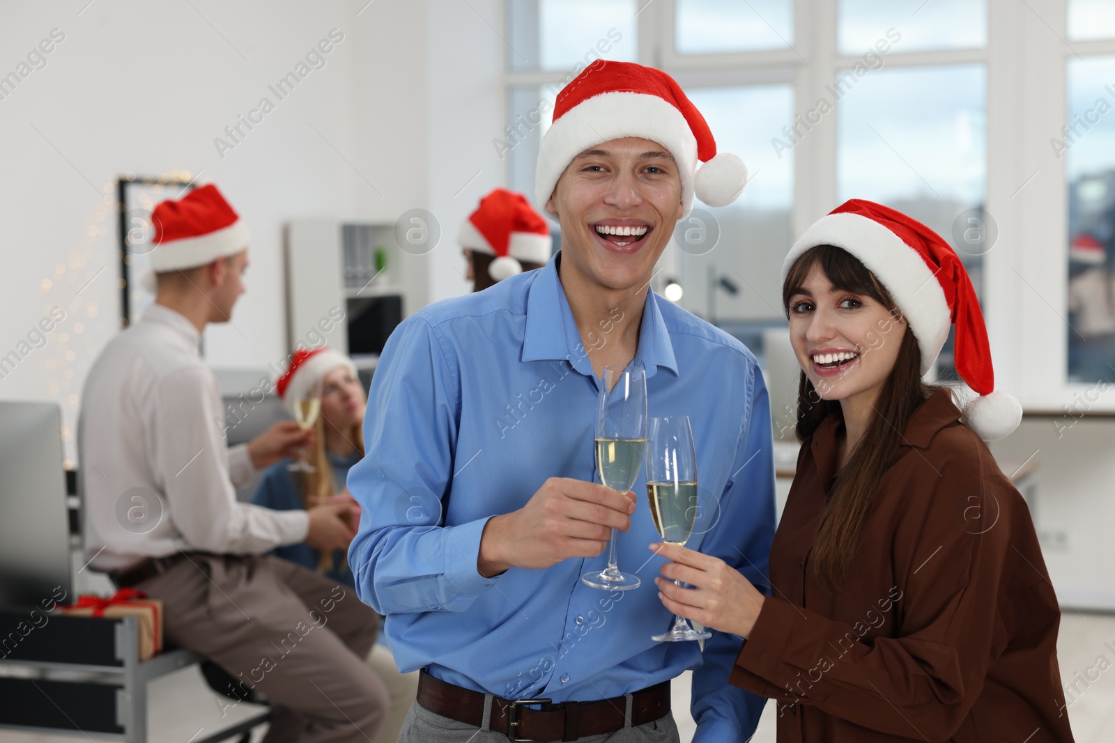 Photo of Smiling colleagues in Santa hats with wine at office Christmas party