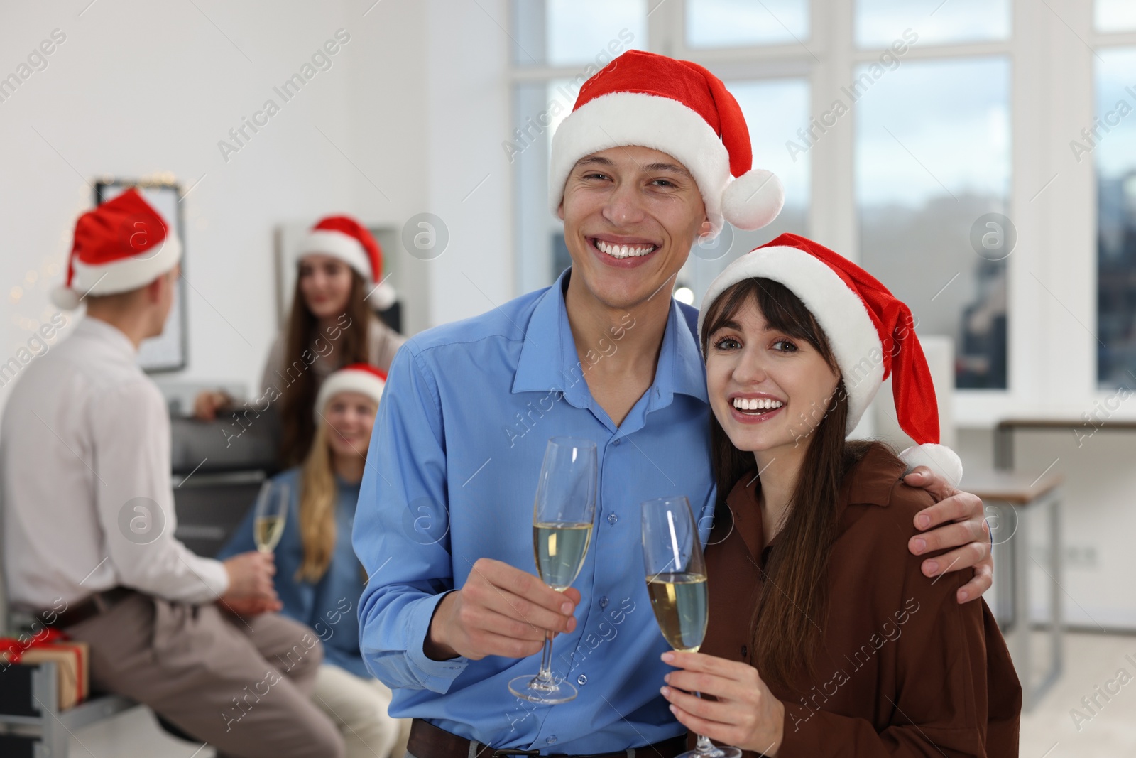 Photo of Smiling colleagues in Santa hats with wine at office Christmas party