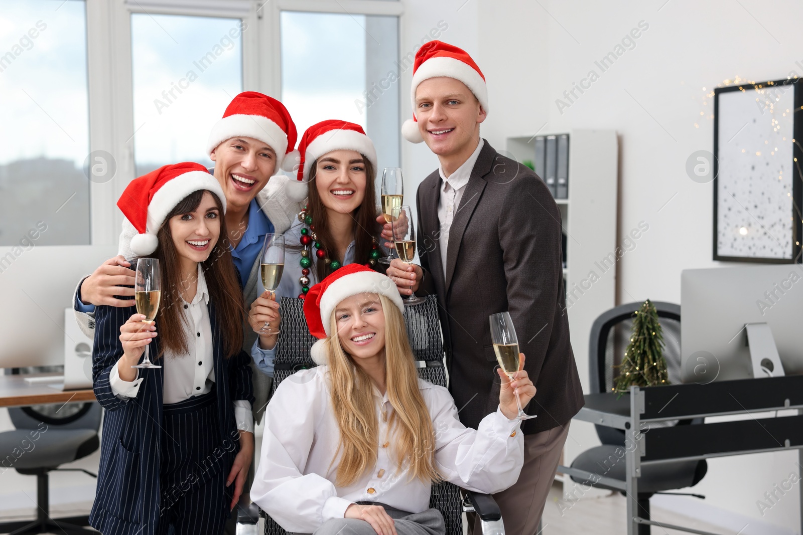 Photo of Cheerful coworkers in Santa hats with glasses of wine at office Christmas party