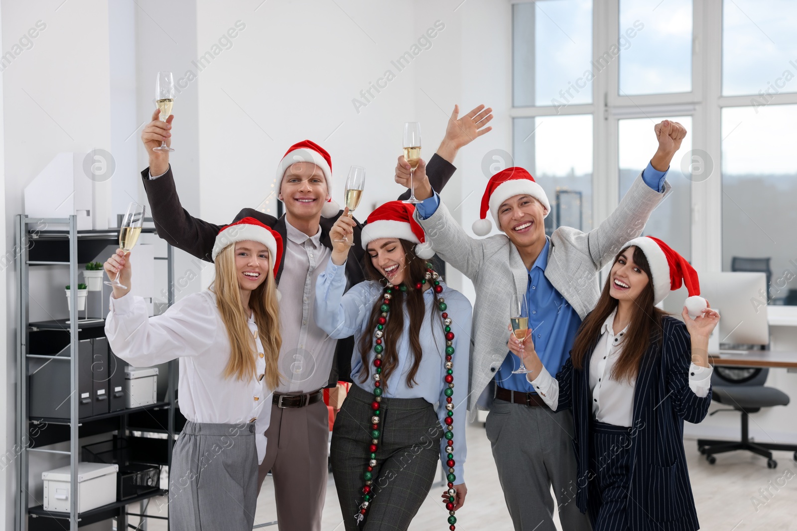 Photo of Cheerful coworkers in Santa hats having fun at office Christmas party