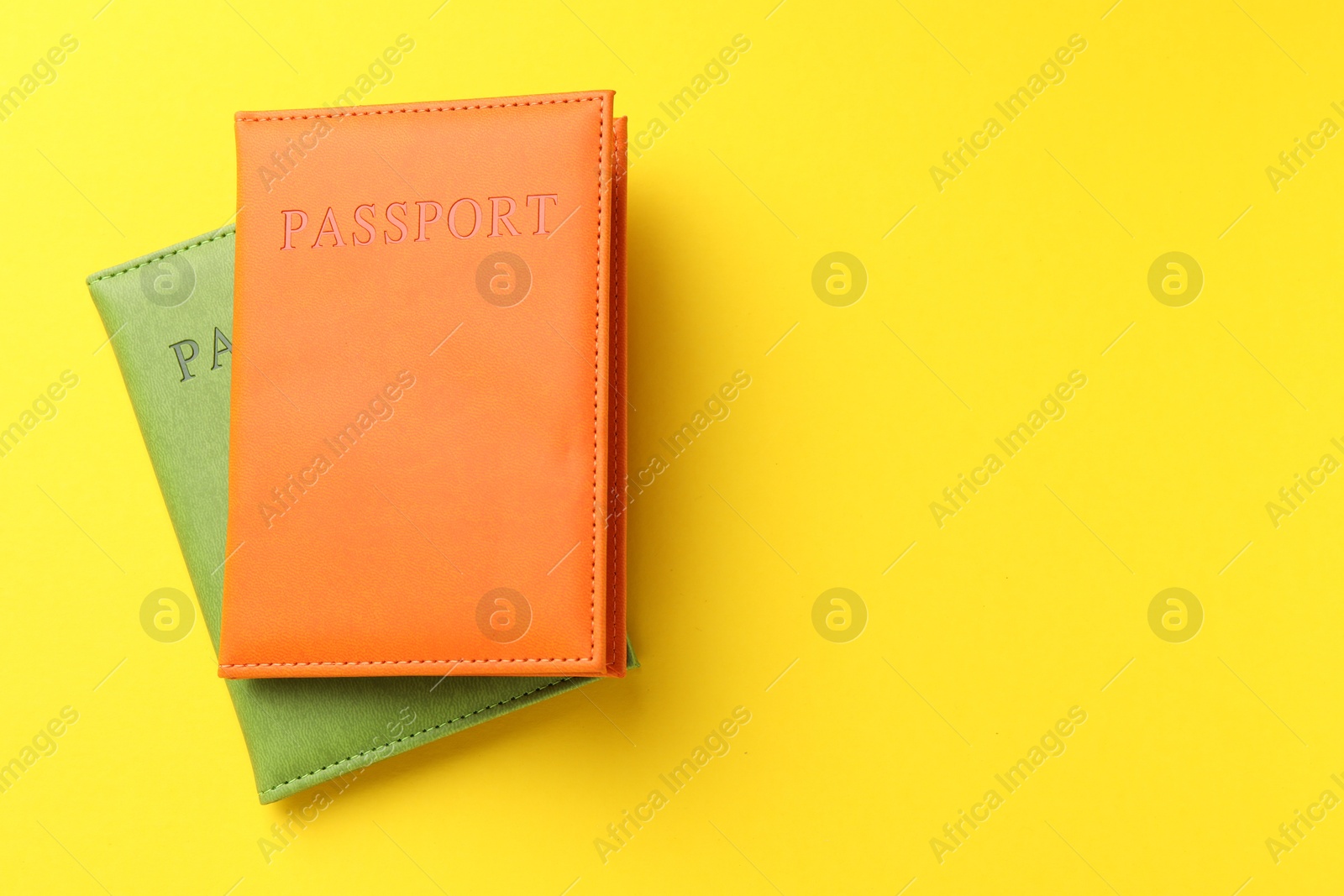 Photo of Passports in color covers on yellow background, top view. Space for text