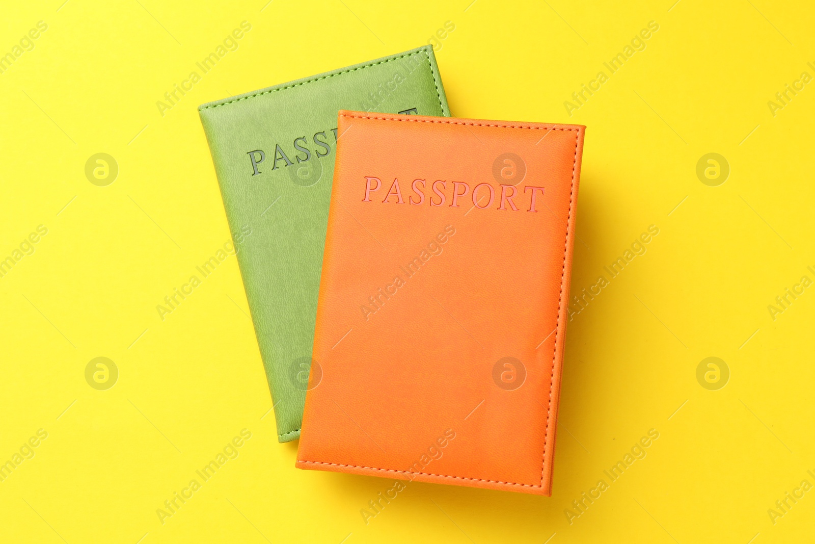 Photo of Passports in color covers on yellow background, top view