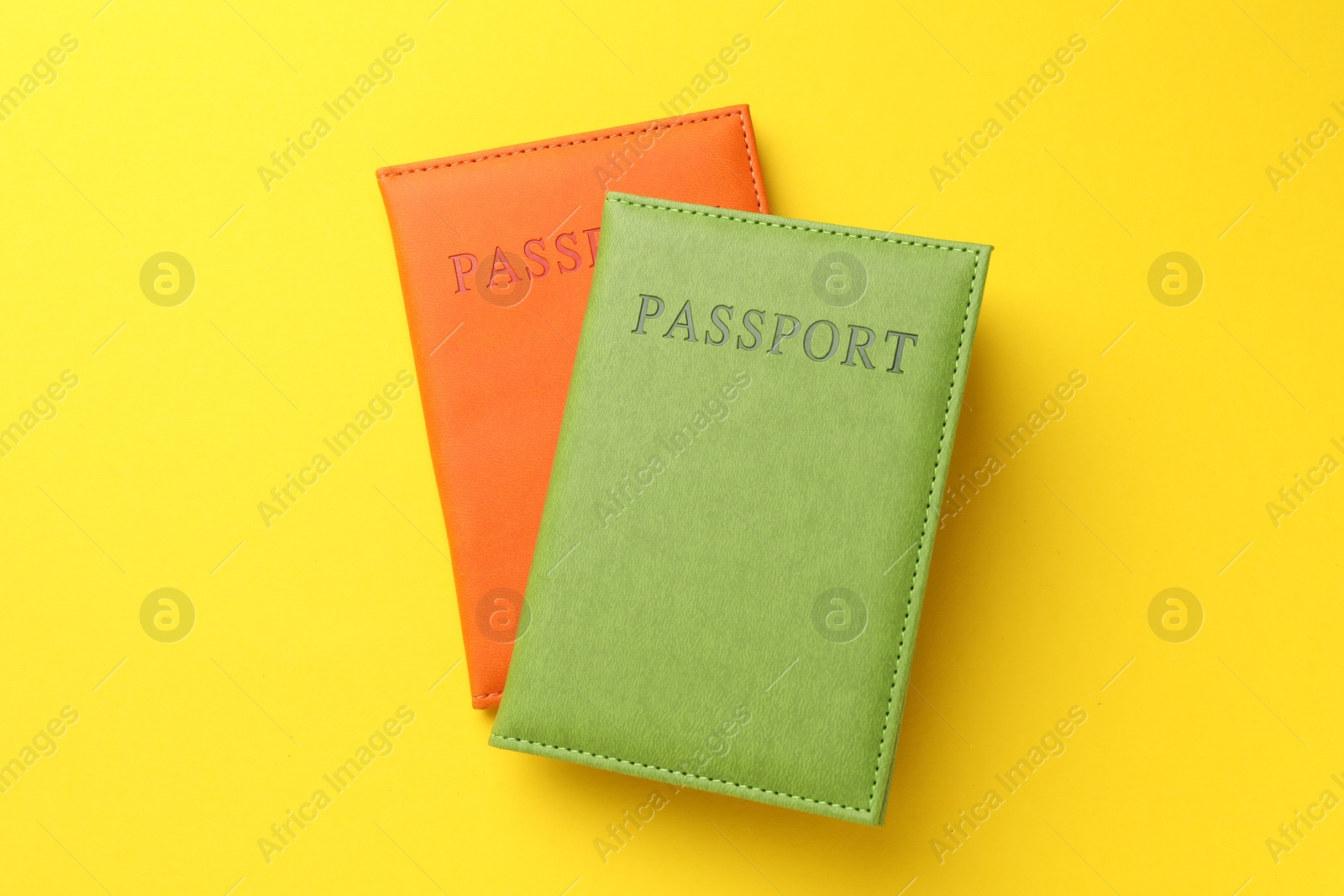 Photo of Passports in color covers on yellow background, top view