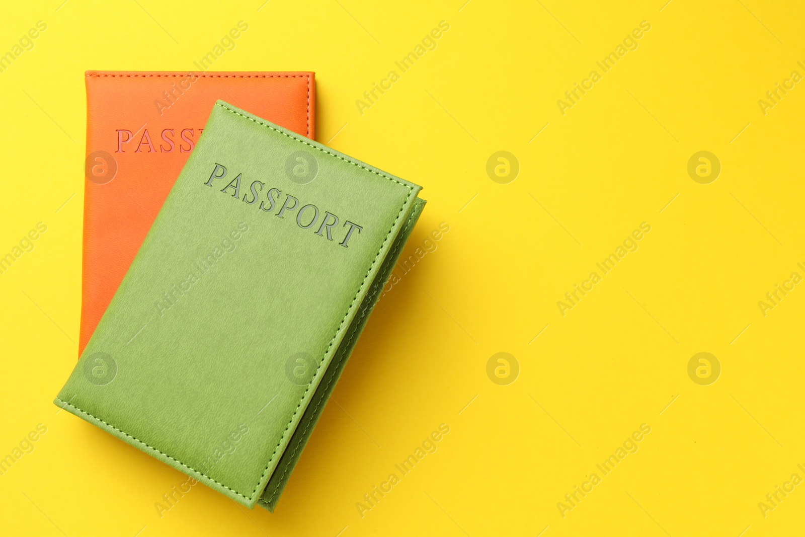 Photo of Passports in color covers on yellow background, top view. Space for text