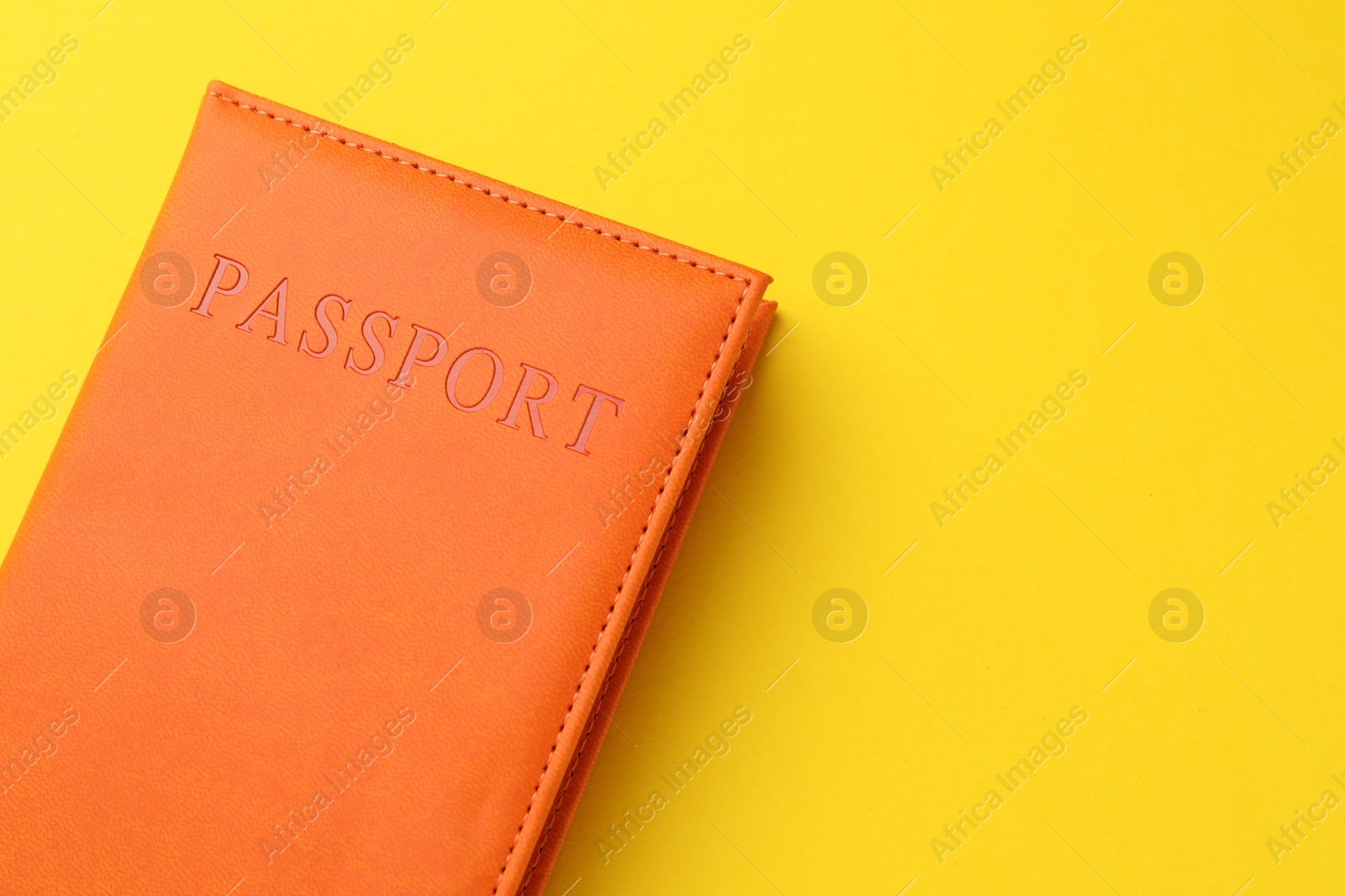 Photo of Passport in orange cover on yellow background, top view. Space for text