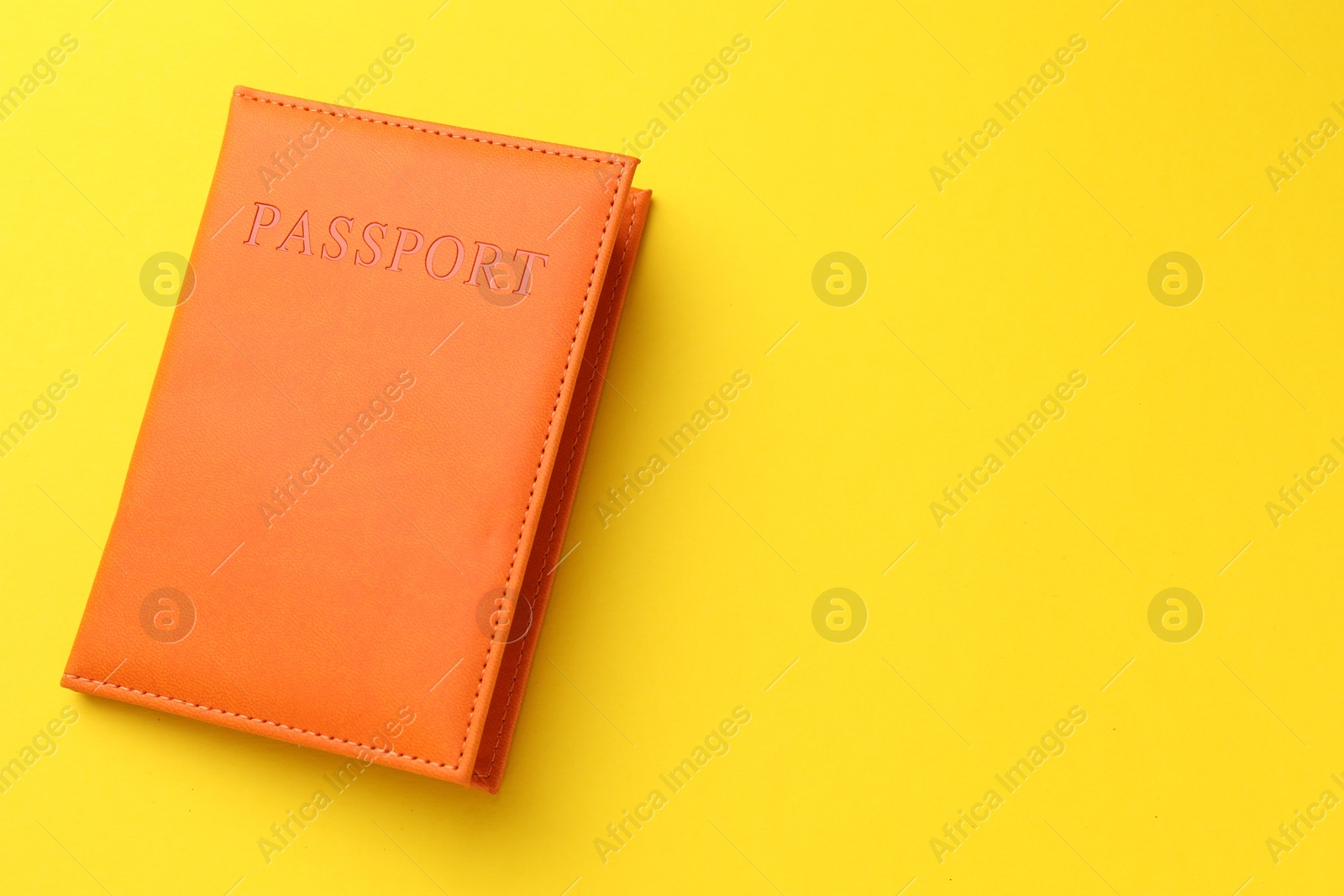 Photo of Passport in orange cover on yellow background, top view. Space for text