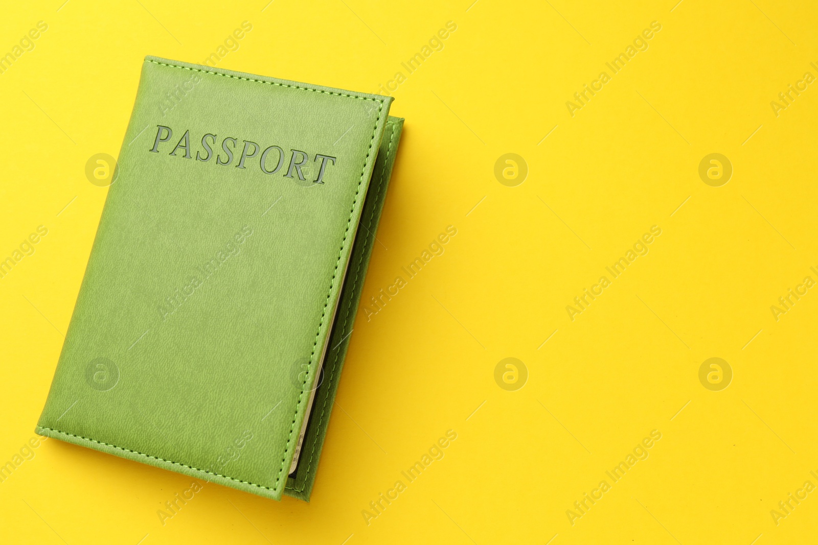 Photo of Passport in green cover on yellow background, top view. Space for text