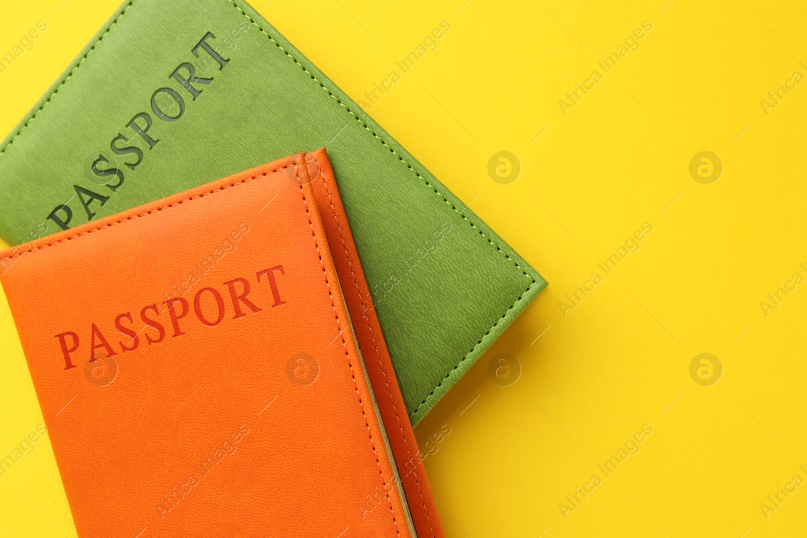 Photo of Passports in color covers on yellow background, top view. Space for text