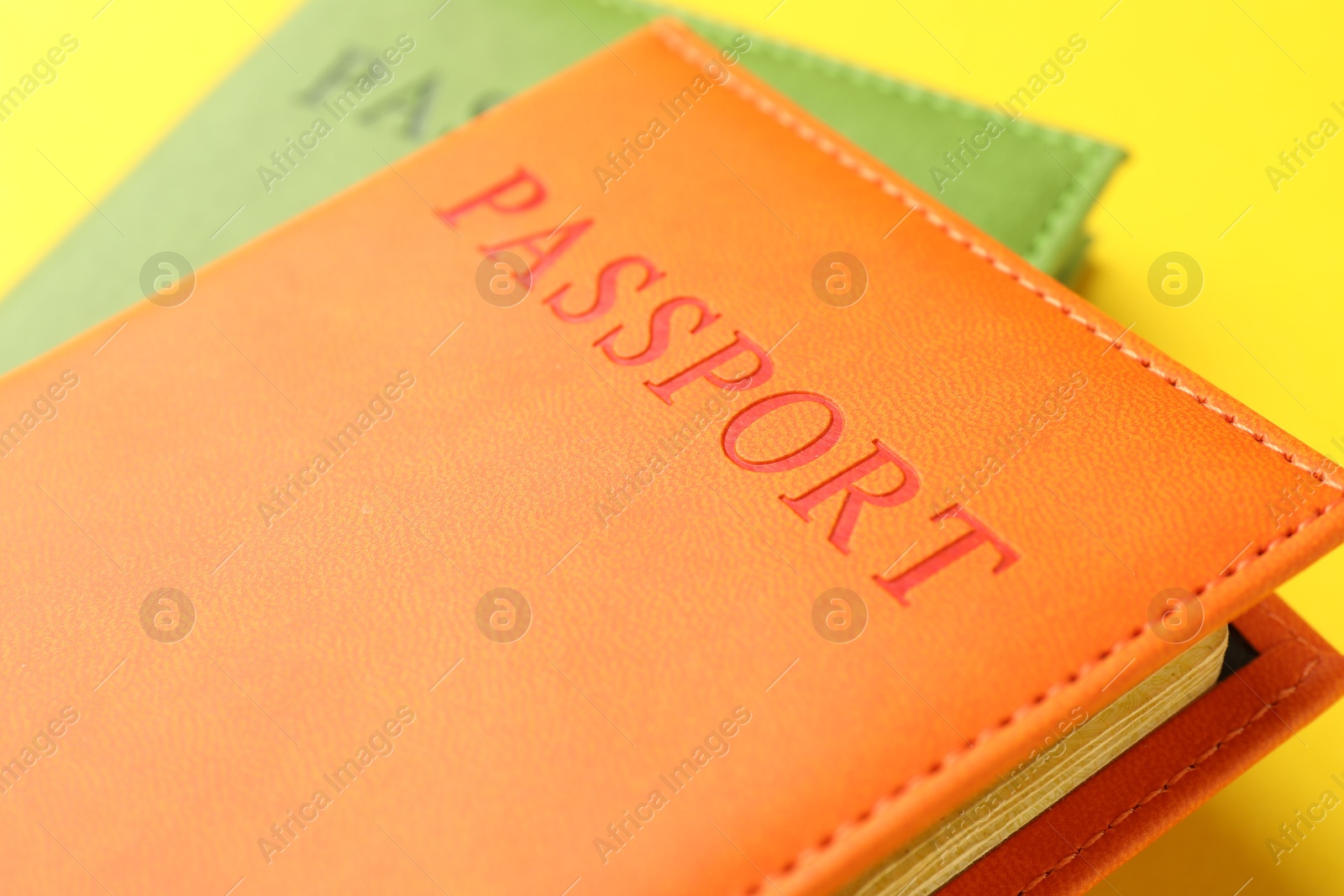 Photo of Passports in color covers on yellow background, closeup