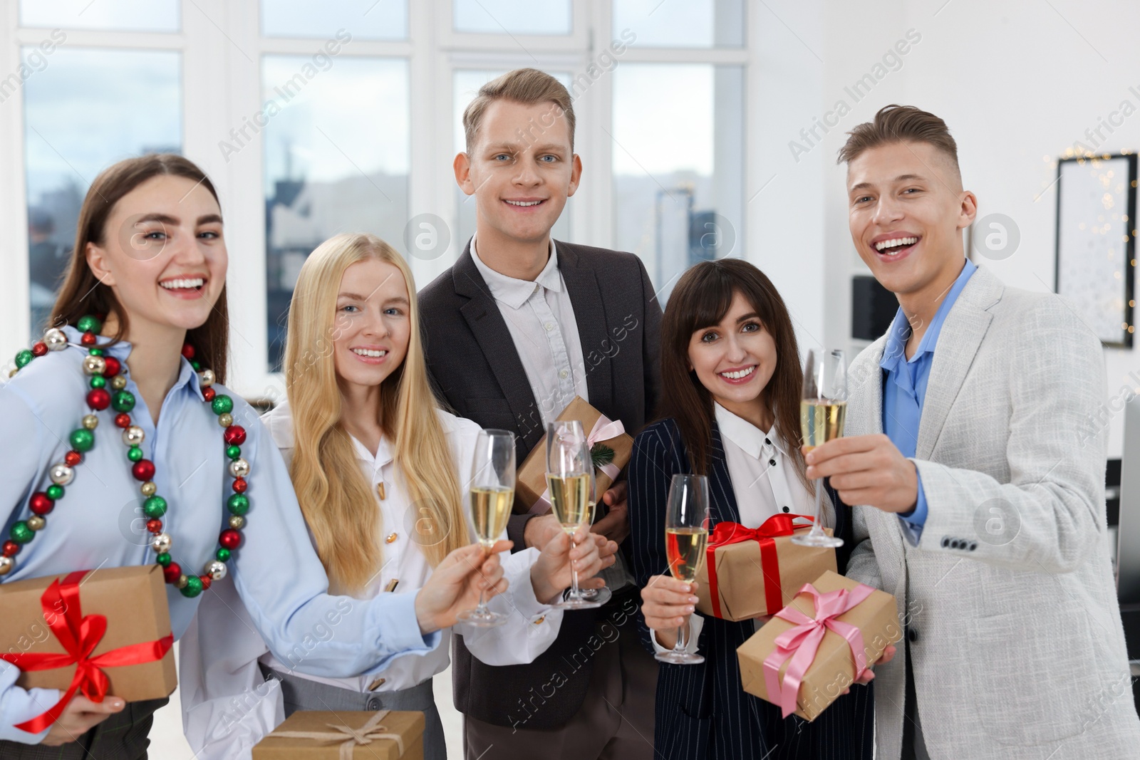 Photo of Cheerful coworkers with gifts and glasses of wine at Christmas party in office