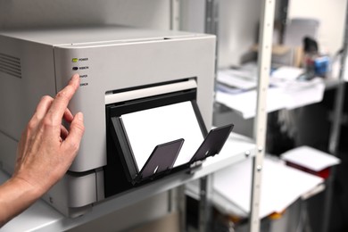 Photo of Woman using modern printer indoors, closeup. Printing house