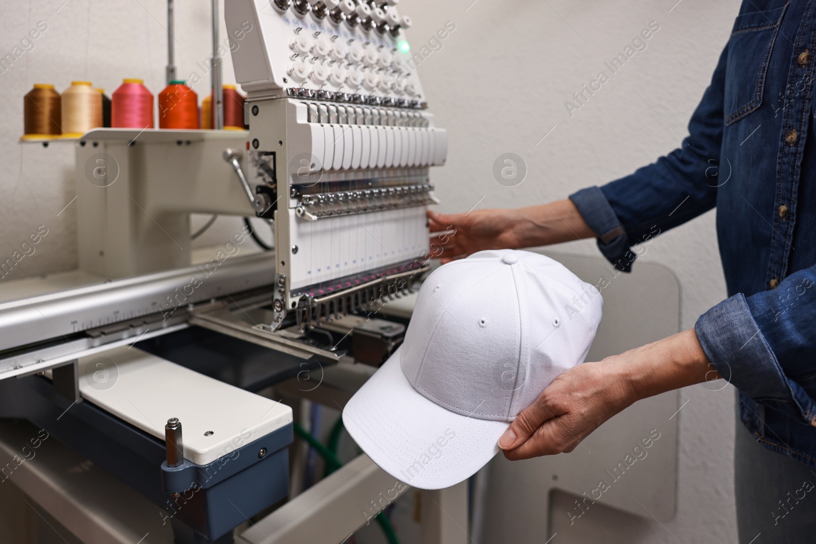 Photo of Woman with blank baseball cap for print using embroidery machine indoors, closeup