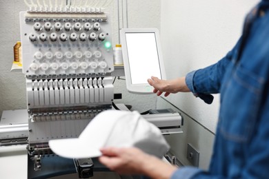 Photo of Woman with blank baseball cap for print using embroidery machine indoors, closeup