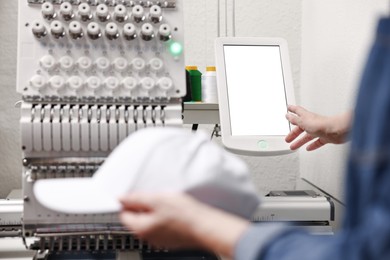 Photo of Woman with blank baseball cap for print using embroidery machine indoors, closeup