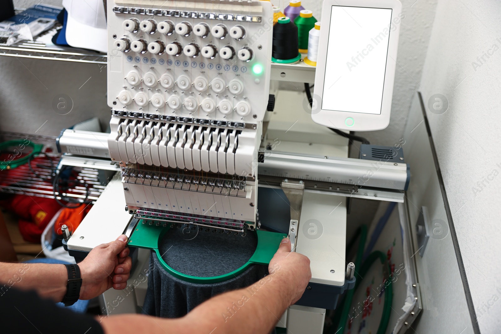 Photo of Man using embroidery machine to make design on T-shirt indoors, closeup