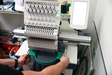 Photo of Man using embroidery machine to make design on T-shirt indoors, closeup