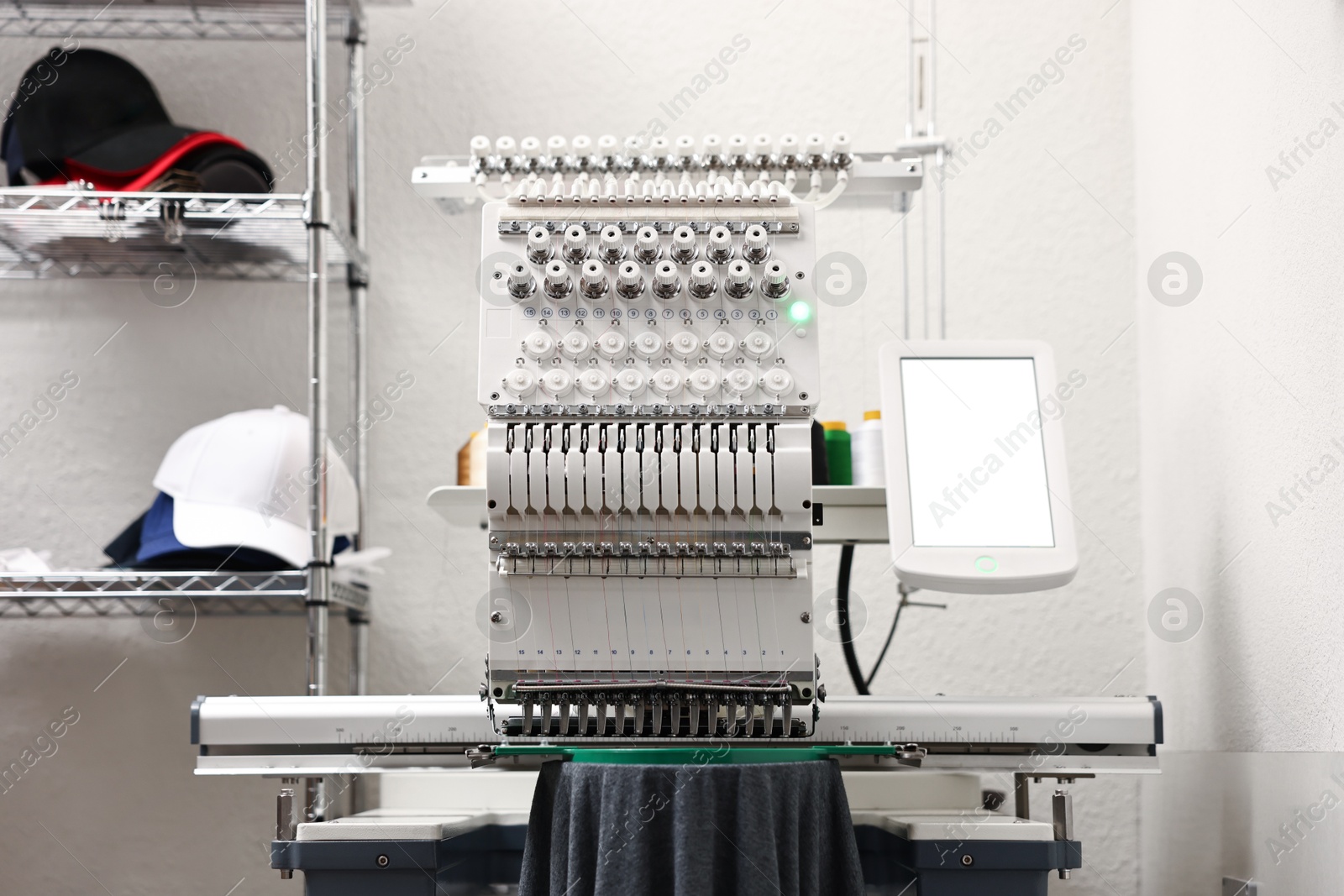 Photo of Modern embroidery machine and stylish caps on rack indoors