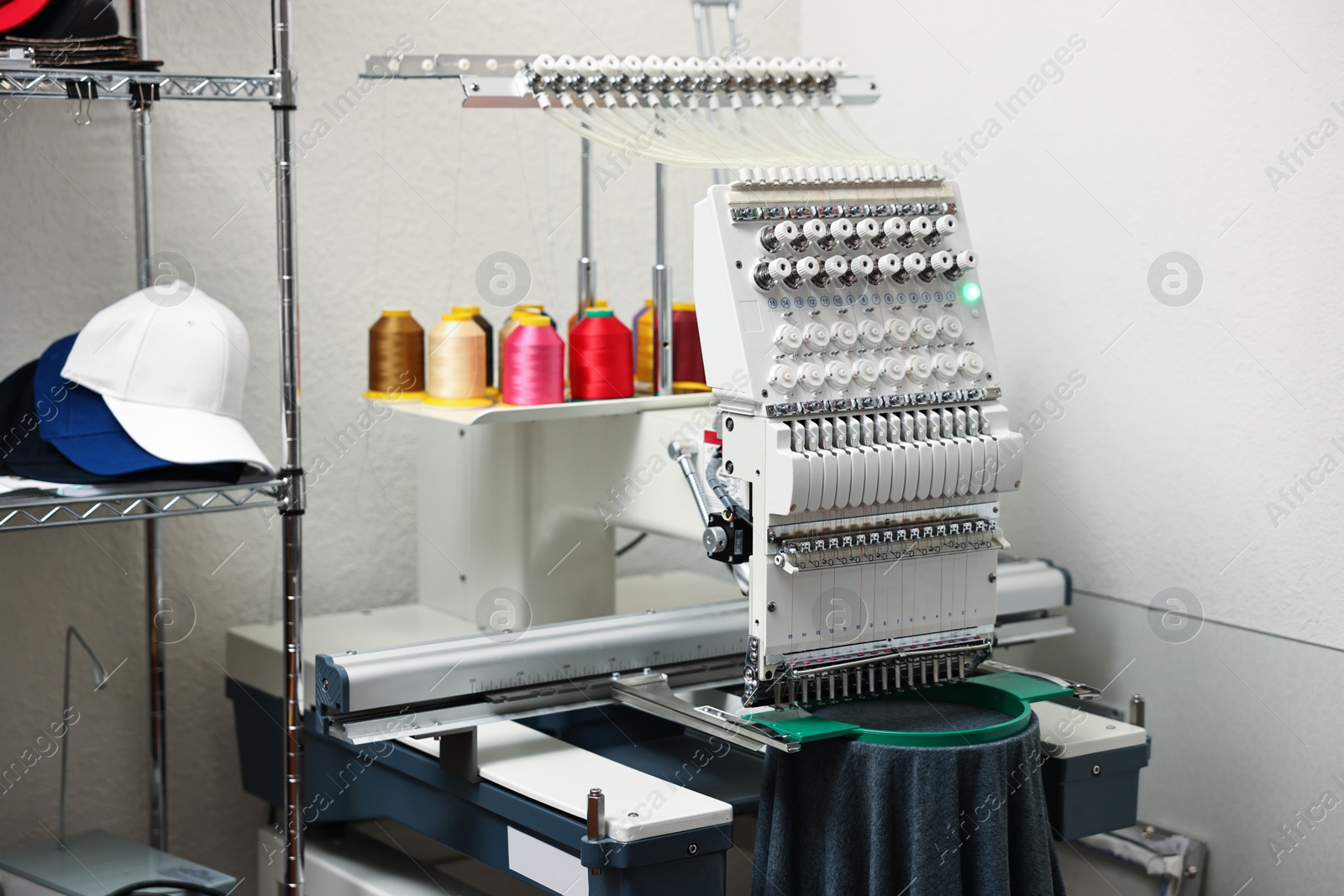 Photo of Modern embroidery machine with spools of thread indoors