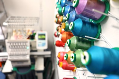 Photo of Spools of thread and modern embroidery machine indoors, selective focus