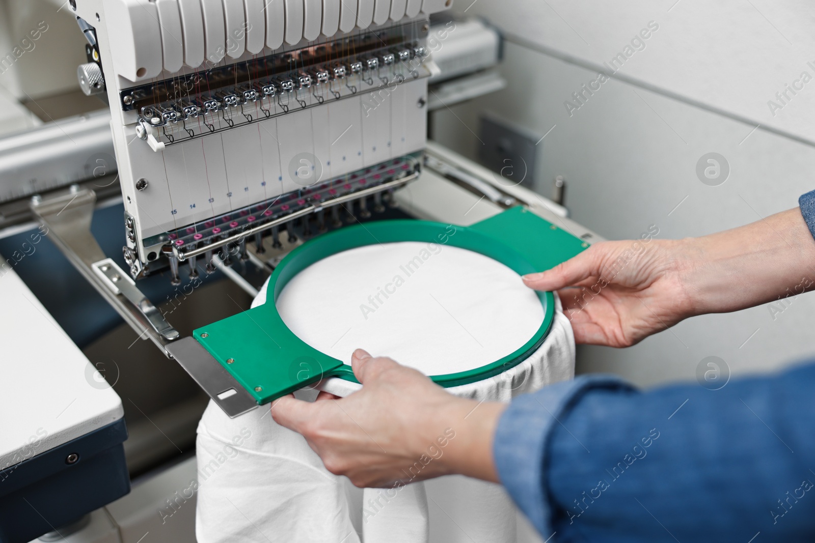 Photo of Woman using embroidery machine to make design on T-shirt indoors, closeup