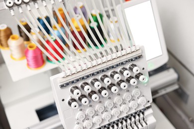 Photo of Modern embroidery machine with spools of thread indoors, selective focus