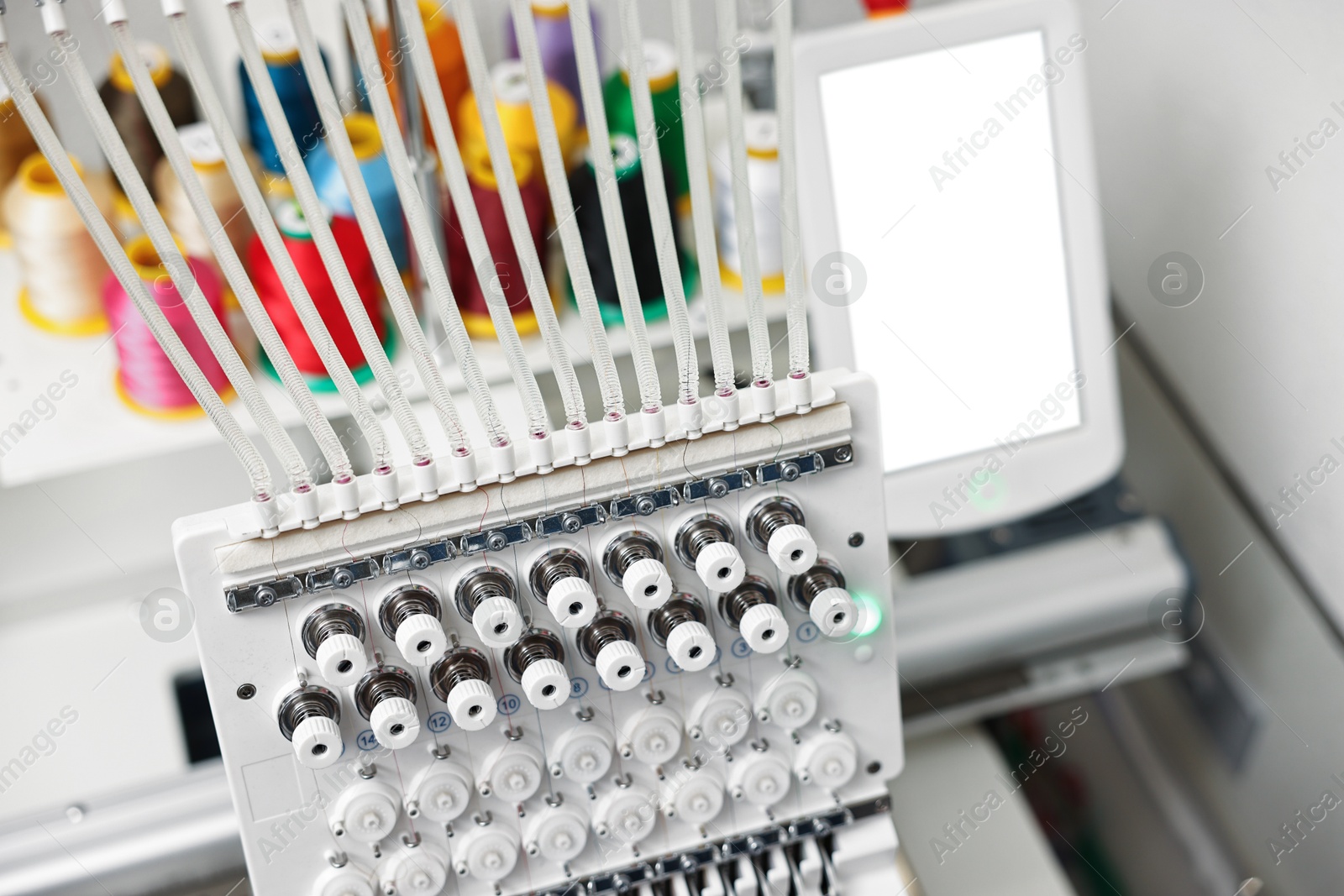 Photo of Modern embroidery machine with spools of thread indoors, selective focus