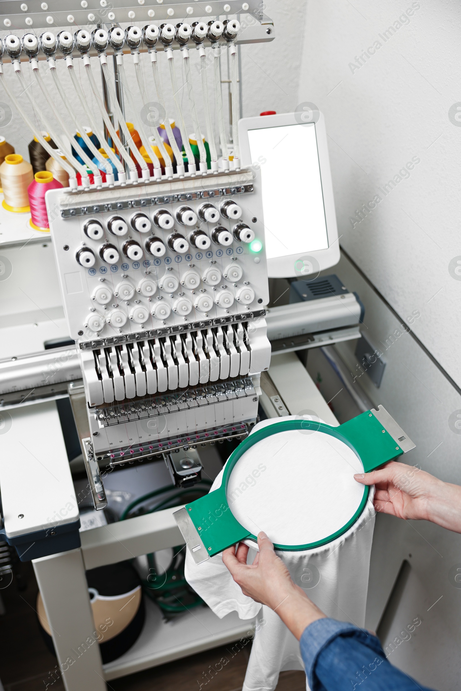 Photo of Woman using embroidery machine to make design on T-shirt indoors, closeup