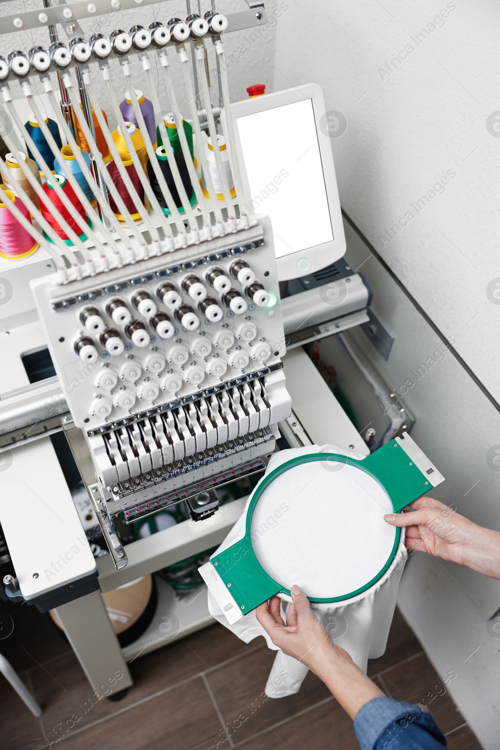 Photo of Woman using embroidery machine to make design on T-shirt indoors, closeup